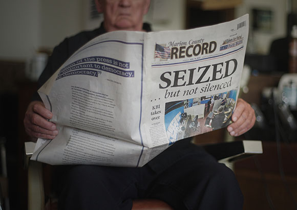 A person holds an open newspaper with the headline SEIZED ... but not silenced.