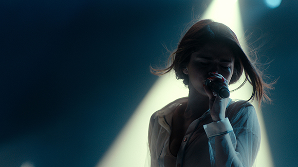 Silhouette of a woman singing into a microphone under a bright spotlight.