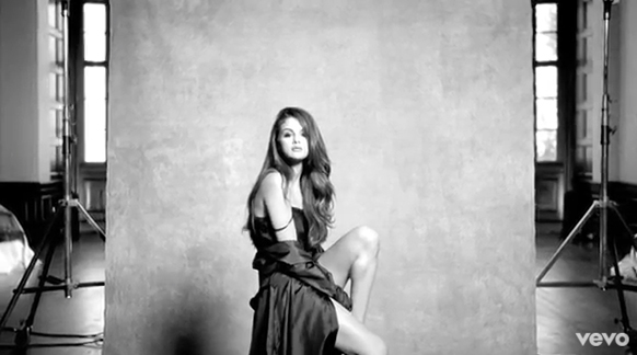 A woman with long hair in a dark dress poses in front of a large, textured studio backdrop.