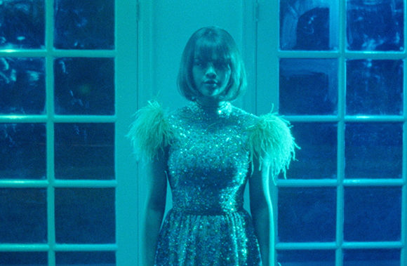 A woman with a bob haircut wearing a sparkling turquoise sequined dress with feather accents.