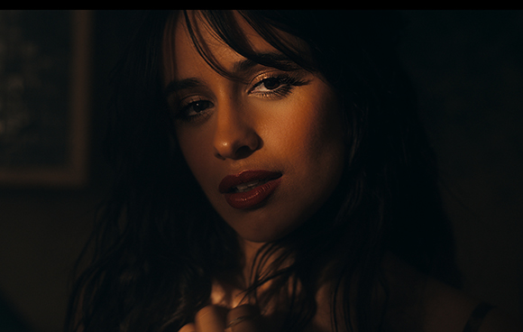 Close-up portrait of a woman with dark hair and red lipstick in warm, dim lighting.