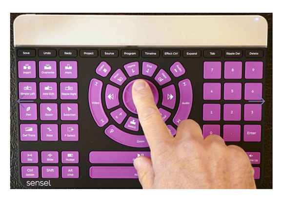 A hand presses a button on a purple specialized video editing controller with various labeled command keys.