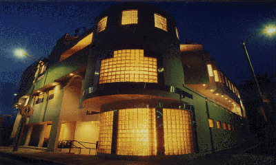 A dark, multi-level building with large, illuminated glass block windows under a night sky.