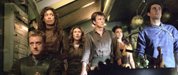 Five people in casual, rugged clothing stand together in a dark, industrial-looking room.