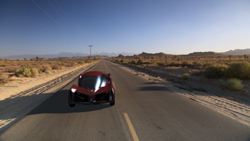 A red futuristic sports car driving down a long, straight asphalt road through a desert landscape.