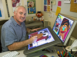 A man sits at a desk using a stylus on a large digital drawing tablet.