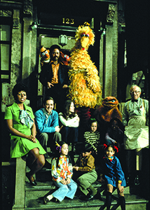 Sesame Street cast members and puppets posing on stone steps in front of a building entrance.