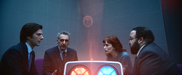 Four people in professional attire lean in to look at a glowing device emitting red and blue light.