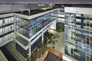 High-angle view of a contemporary glass-walled office building with illuminated windows at night.