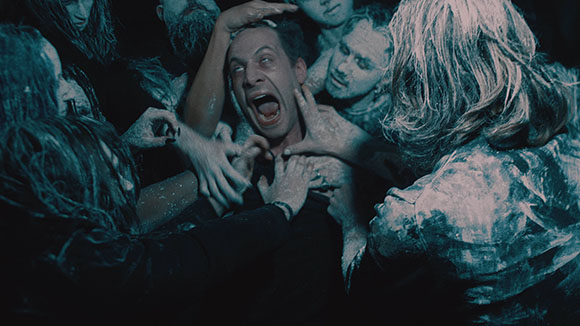 A man screams as several people covered in white powder surround and grab him in a dark setting.