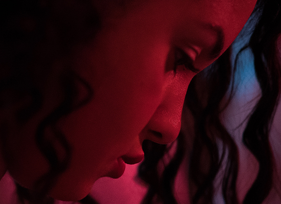 Close-up profile of a person with curly hair illuminated by deep red light.