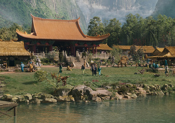 Traditional East Asian temple with orange tiled roofs nestled in a green valley by a lake.