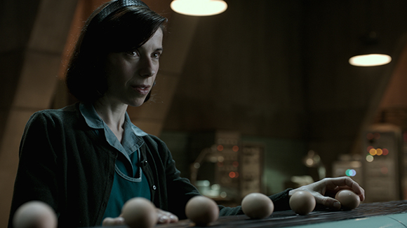 A woman with dark hair looks down at a row of eggs on a dark table in a dimly lit room.