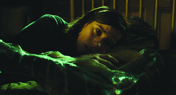 A person with dark hair lies in a dark room illuminated by a green light.