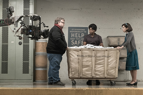 A man and a woman stand on either side of a large laundry cart filled with white linens.
