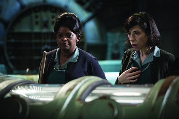 Two women in mid-century clothing look with concern at a glowing, curved industrial machine.