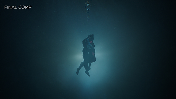 Two figures in dark clothing embrace and float underwater, illuminated by a bright light from below.