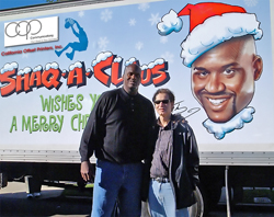 Two people pose in front of a white truck featuring a large cartoon illustration of a man in a Santa hat.