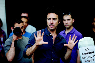 A man in a dark blue shirt holds his hands up in a gesture while standing in a crowd.