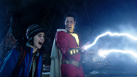 A boy in a blue jacket and a man in a red superhero costume smile as a bolt of lightning streaks past.