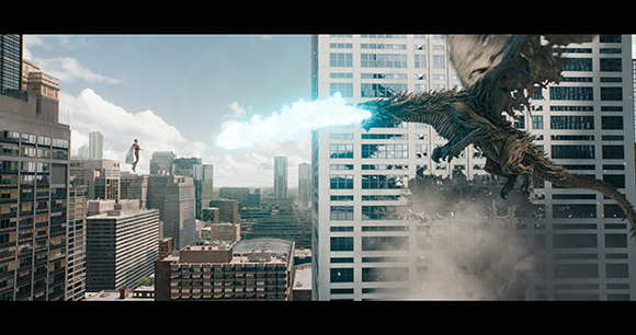A large dragon breathes blue fire toward a tall building in a dense cityscape.
