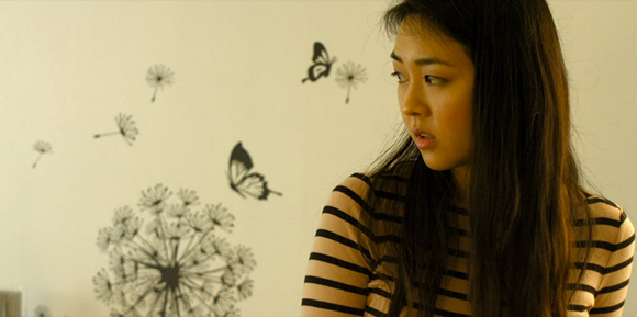 A young woman with long dark hair wearing a striped shirt looks to the side in front of wall decals.