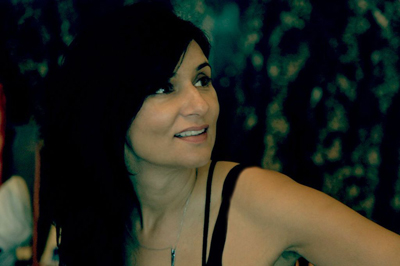 A woman with long dark hair smiling and looking off-camera against a dark, textured background.