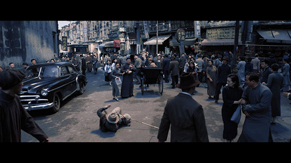 A busy historical street with people, a black vintage car, a rickshaw, and a man lying on the pavement.