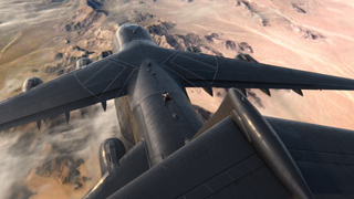 High-angle view looking down the fuselage and wings of a large grey military aircraft over desert terrain.