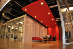 A modern office space featuring a large, rectangular red ceiling panel with recessed lights over a seating area.