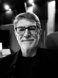 Black and white close-up portrait of a smiling man with glasses and a graying beard.