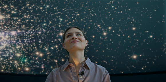 A smiling woman looks upward against a dark background filled with many bright, glowing stars.