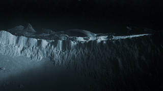 A dark, monochromatic view of a jagged, rocky ridge under dim light.