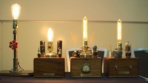 Four glowing Edison-style light bulbs in various decorative wooden and metal bases on a dark surface.