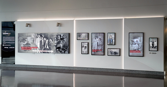 A long, backlit wall display featuring various black and white historical photographs and text panels.