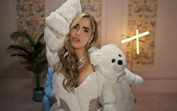A woman with long blonde hair wearing a white faux fur outfit and holding a large white teddy bear.