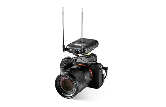 A black DSLR camera with a large lens and a wireless transmitter with two antennas mounted on the hot shoe.