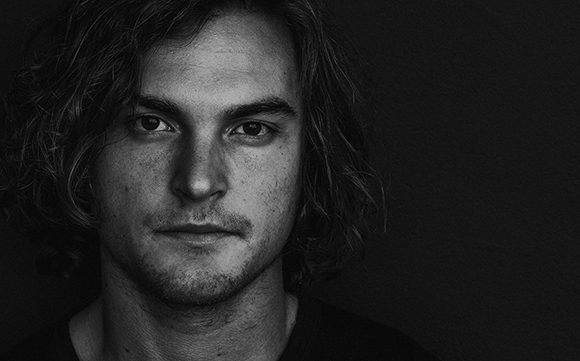 Black and white close-up portrait of a man with wavy hair looking directly at the camera.