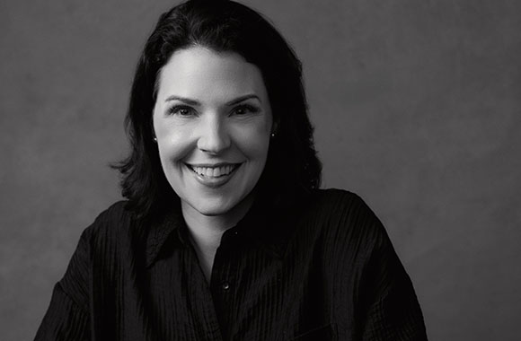 Black and white portrait of a smiling woman with dark hair wearing a dark button-down shirt.