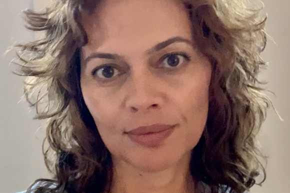 A woman with wavy, light brown hair and highlights looks directly at the camera.