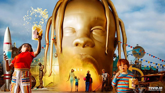 A massive golden head with dreadlocks towers over people in a colorful, surreal outdoor setting.
