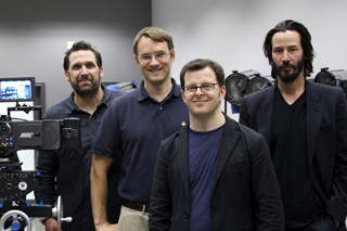 Four men standing in a studio near a professional film camera and lighting equipment.