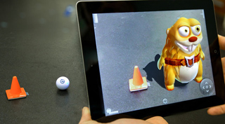 A tablet displays a 3D cartoon creature and a digital cone overlaid on a real orange cone on a dark surface.