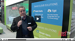 A man in a black suit speaks into a microphone in front of a large sign for cloud solutions.