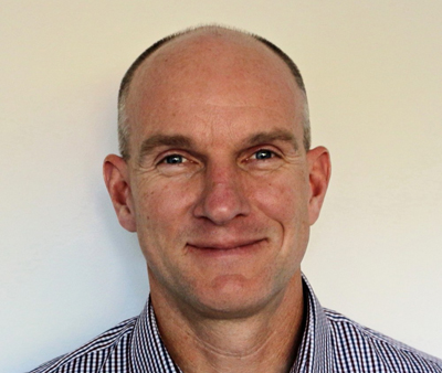 A smiling man with a shaved head wearing a checkered button-down shirt against a white background.