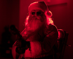A person in a Santa Claus costume and sunglasses under intense red light.