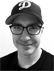 Black and white headshot of a man wearing a baseball cap with a letter D and dark-rimmed glasses.