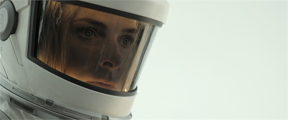 Close-up of a person's eyes and face visible through the clear visor of a white space helmet.