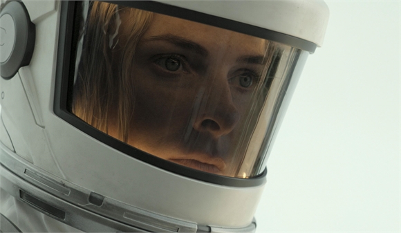 Close-up of a person's face visible through the visor of a white astronaut helmet.