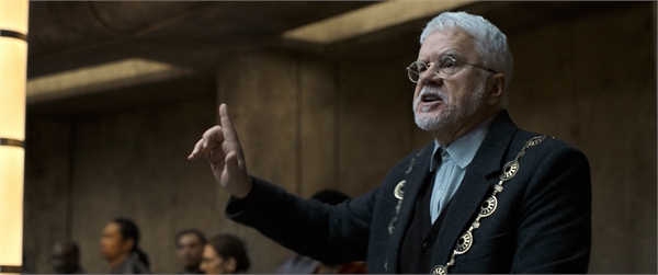 An older man with white hair and glasses gestures with his index finger raised during a speech.